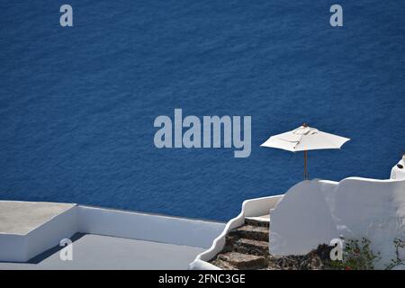 Paysage pittoresque avec un parasol blanc isolé contre le bleu de la mer Égée dans l'île de Santorin, Cyclades Grèce. Banque D'Images