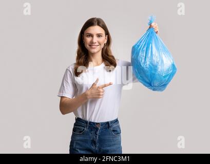 Portrait de la jeune femme souriante qui pointe vers Blue Plastic Sac poubelle Banque D'Images