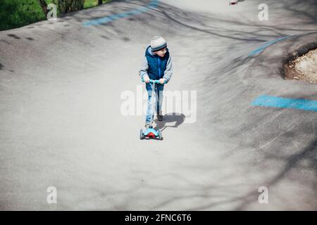 Un petit garçon fait un scooter sur les routes de la aire de jeux Banque D'Images