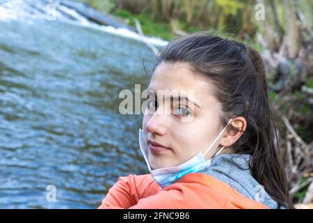 Portrait d'une jeune fille adolescente souriant et avec elle Masque par le Covid19 abaissé respirant de l'air frais dans la nature à côté d'un jet d'eau avec copie sp Banque D'Images