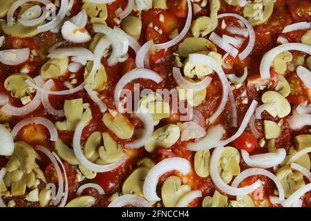 Vue de dessus sur une pizza fraîche et non cuite végétalienne préparée avec des ingrédients de base sauce tomate, oignons et champagnes Banque D'Images