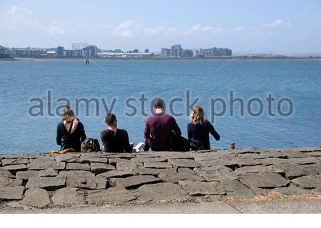 Édimbourg, Écosse, Royaume-Uni. 16 mai 2021. Les gens qui profitent de l'extérieur au bord de l'eau du port de Newhaven, dans un après-midi chaud et ensoleillé au printemps. Vue sur le quatrième estuaire vers le développement moderne à Granton. Crédit : Craig Brown/Alay Live News Banque D'Images