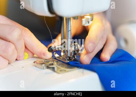 Gros plan de couture sur mesure ou de couture de couture ou de couture de tissu bleu marine avec une machine professionnelle tout en étant assis et en faisant de nouveaux vêtements à son lieu de travail dans l'atelier ou l'atelier, foyer sélectif Banque D'Images