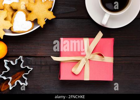 Une tasse de café et un cadeau rose avec un ruban beige sur une table sombre. Banque D'Images