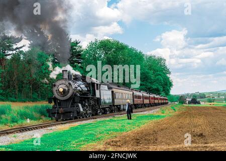 Strasburg, PA, USA - 15 mai 2021 : un homme Amish regarde une locomotive à vapeur de la route ferroviaire de Strasburg se prépare à s'éloigner d'une plantation de pique-nique dans r Banque D'Images