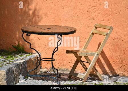 Terrasse de galets de café local avec table de bistro et chaise pliante en bois contre un mur de stuc rose saumon vénitien dans le Real de Catorce, Mexique. Banque D'Images