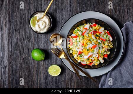 Salade de crabe de bâtonnets de surimi aux légumes : maïs, concombres, scallion, œufs, riz jasmin avec sauce lime et mayonnaise servi dans un bol noir o Banque D'Images