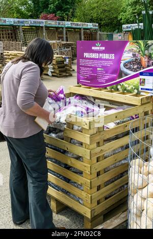 Une femme regardant des sacs de galets polis décoratifs à vendre dans un centre de jardin. Banque D'Images