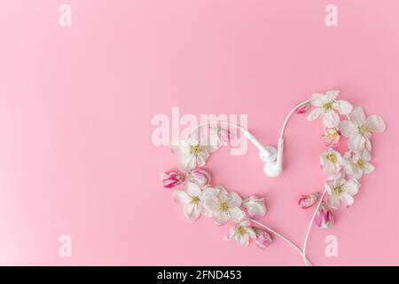 Flat Lay sur fond rose avec la forme de coeur de fleur de pomme et écouteurs Banque D'Images