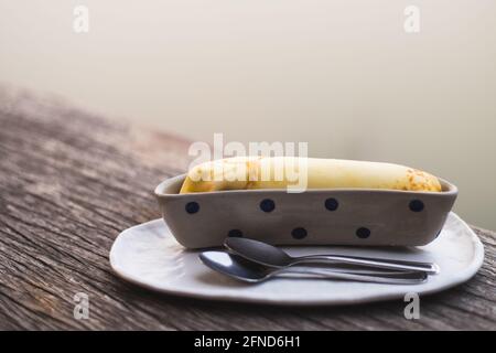 Banane crêpe sucrée dessert objet encore vie. La crêpe mise dans le récipient en céramique bol forme banane. Banque D'Images