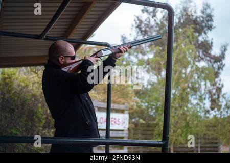 Bald homme portant des lunettes de soleil de sécurité et des écouteurs tenant un fusil de chasse, en tirant des cibles en argile dans l'ouverture. S'entraîner pendant l'hiver au Royaume-Uni avec un bea Banque D'Images