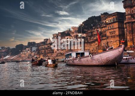 Varanasi, Inde - 01 novembre 2016 : coucher de soleil spectaculaire dans un lieu de culte hindou sacré avec beaucoup de touristes sur les bateaux et l'ancienne architecture ghat loc Banque D'Images