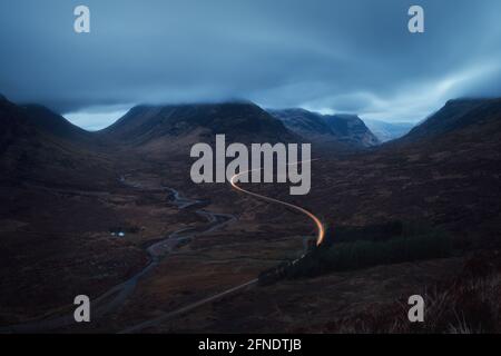 Paysage du matin avec feux de voiture sur la route de montagne menant à Glencoe en face de Buachaville Etive Mor. A82 route avant l'aube. Écosse Banque D'Images
