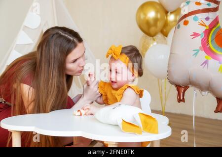 Le mama caucasien apaise et embrasse une fille d'un an qui pleure, photo studio pour un enfant d'un an Banque D'Images