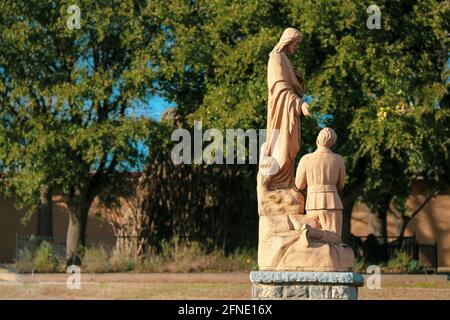 cimetière cimetière avec ancienne prière priant stature avec arbres luxuriants au-delà dans une scène religieuse solennelle Banque D'Images