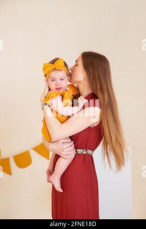 Maman apaise et embrasse une fille d'un an qui pleure, photo studio pour un enfant d'un an Banque D'Images