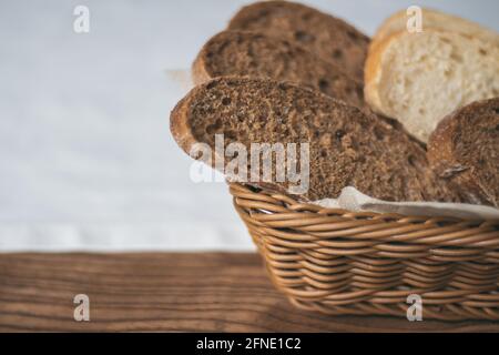 Panier en osier partiellement flou avec pain noir et blanc nappe blanche sur table en bois Banque D'Images