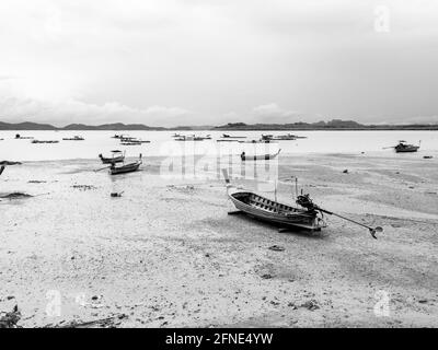 Bateau de pêche à longue queue en bois de villageois vides dans la boue de plage près de la mer avec des bateaux flottants près de l'île dans le style noir et blanc. Pêcheur thaïlandais Banque D'Images