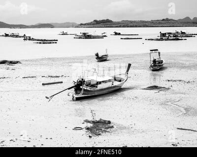 Bateau de pêche à longue queue en bois de villageois vides dans la boue de plage près de la mer avec des bateaux flottants près de l'île dans le style noir et blanc. Pêcheur thaïlandais Banque D'Images