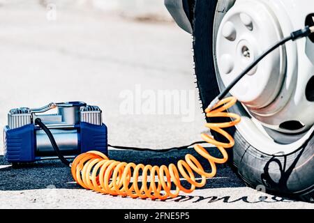 La pompe électrique du compresseur gonfle le pneu crevé de la voiture. Assistance routière et dépannage en cours de route. Gros plan avec espace à copier. Banque D'Images