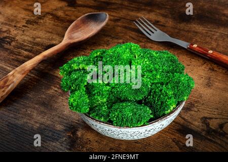 Brocoli bouilli dans un bol sur fond de bois rustique foncé avec une fourchette. Accompagnement végétalien biologique sain Banque D'Images