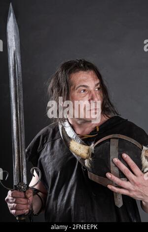 knight tient un casque à cornes et une épée dans son mains sur fond sombre Banque D'Images