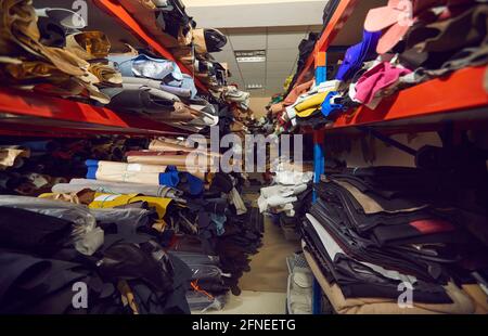 Allée entre les tablettes avec beaucoup de rouleaux de tissu et de cuir à l'usine de chaussures ou de vêtements Banque D'Images