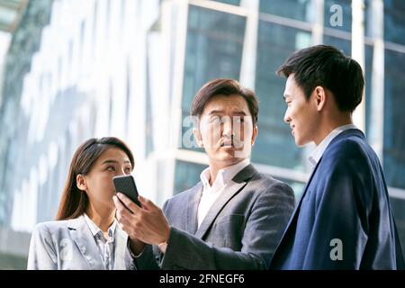 une équipe d'hommes d'affaires asiatiques debout dans la rue ayant une discussion en utilisant le téléphone cellulaire dans le centre-ville Banque D'Images