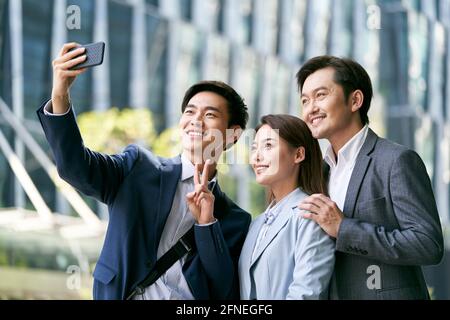 équipe de trois hommes d'affaires asiatiques prenant un selfie à l'extérieur dans le quartier financier de la ville Banque D'Images