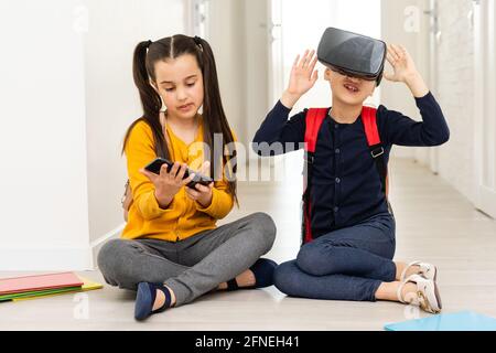 Sur toute la longueur de deux écolières multiculturelle tenant la main pendant l'utilisation de casques de réalité virtial sur fond blanc Banque D'Images