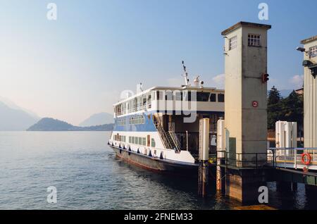 En début de matinée, vue sur le lac de Côme avec un ferry amarré dans le port de Menaggio, en Italie, et ciel clair, avec brouillard, lumière du soleil et montagnes dans le Banque D'Images