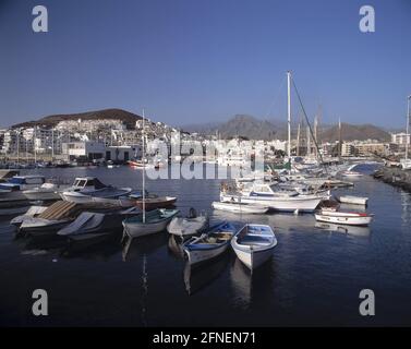 Les bateaux à rames et à voile sont amarrés dans le port de plaisance de Los Christianos. En arrière-plan les hôtels touristiques typiques des îles Canaries. [traduction automatique] Banque D'Images