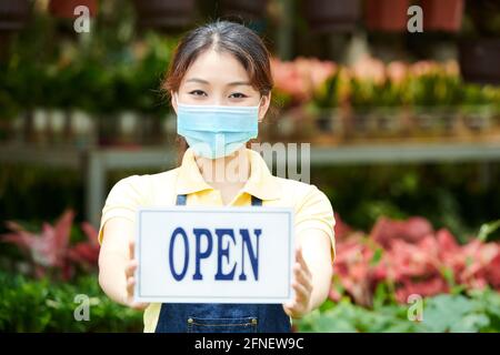 Portrait de jeune femme gaie dans un masque médical montrant ouvert signez et invitez les clients à planter une pépinière Banque D'Images