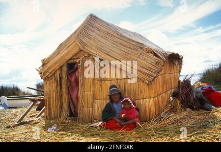 Une famille Indio en face de leur cabane de chaume sur une île uro dans le lac Titicaca. Les îles uro sont des îles flottantes faites de roseaux, du nom des Indiens qui y vivaient autrefois. Les Indiens qui y vivent aujourd'hui sont un mélange de descendants d'uro, d'Aymará et d'Inca. [traduction automatique] Banque D'Images