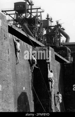 Vue des hauts fourneaux désutilisés des aciéries de fer et d'acier de Meiderich à Duisburg en juillet 1991. Au premier plan, un groupe d'hommes monte les murs d'escalade nouvellement installés. Ils sont situés dans les vieux bunkers de charbon, les zones de stockage de charbon près des hauts fourneaux. Les murs d'escalade ont été créés dans le cadre de la transformation de l'ancienne zone industrielle en parc paysager Duisburg-Nord. [traduction automatique] Banque D'Images