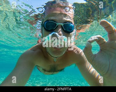 Vue sous-marine d'un plongeur jeune homme nager dans la mer. Des bulles d'air sortant de la bouche et le nez Banque D'Images