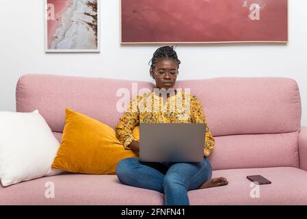 Bussineswoman noir concentré indépendant travaillant sur le projet de démarrage et assis sur le canapé dans la salle de séjour Banque D'Images