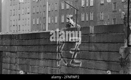 Berlin-City / GDR / 20.3.1980 Bernauer Strasse in Wedding. Les anciennes pierres murales sont remplacées par des éléments en forme de L en béton lisse. Le jeune garde-frontière est là pour surveiller les ouvriers de la construction. Pour les empêcher de fuir vers l'Occident. Du côté ouest, quelqu'un a écrit -KZ- sur le mur. Derrière le mur se trouve Berlin-Mitte. // RDA / mur / districts / Stasi / Histoire / communisme [traduction automatique] Banque D'Images