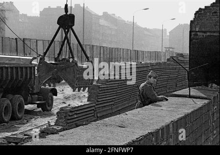 Berlin-City / GDR / 20.3.1980 Bernauer Strasse in Wedding. Les anciennes pierres murales sont remplacées par des éléments en forme de L en béton lisse. Le jeune garde-frontière est là pour surveiller les ouvriers de la construction. Pour les empêcher de fuir vers l'Occident. // RDA / mur / districts / Soldat / Histoire / communisme [traduction automatique] Banque D'Images