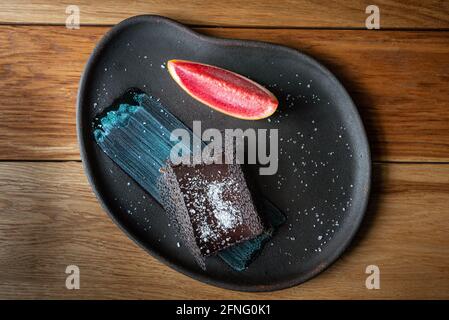 Dessert au chocolat avec glace au pamplemousse servi sur une assiette noire. Pâtisserie et dessert sur fond de bois. Dessert raffiné, brownie au chocolat. Vue de dessus. Banque D'Images
