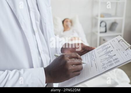Gros plan du médecin africain écrivant la prescription en carte médicale pour patient allongé en arrière-plan Banque D'Images