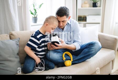 Père avec le syndrome de Happy Down fils à l'intérieur à la maison, à l'aide de lunettes vr. Banque D'Images