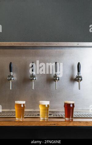 Différents types de bière avec mousse en verre cruches contre rangée de tarauds dans la barre sur fond gris Banque D'Images