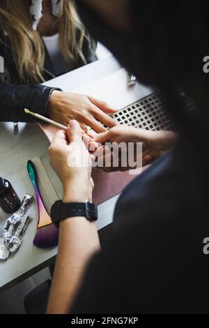 Grand angle de la récolte anonyme maître de beauté clouer de la femme utilisant le tableau d'émeri pendant la procédure de manucure à la table Banque D'Images