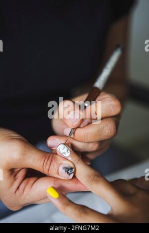 Par-dessus la récolte manucuriste méconnaissable faisant l'art des ongles pour femme dans le salon de beauté en plein jour Banque D'Images