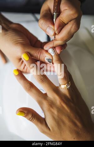 Par-dessus la récolte manucuriste méconnaissable faisant l'art des ongles pour femme dans le salon de beauté en plein jour Banque D'Images