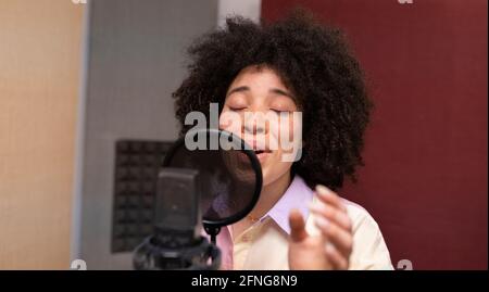 Une chanteuse noire interprète une chanson contre un microphone avec filtre pop lorsque vous êtes debout et que vous fermez les yeux sur le studio audio Banque D'Images
