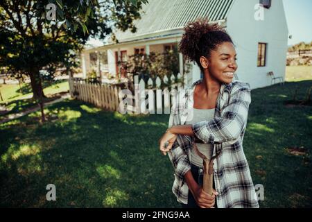 Femme afro-américaine debout dans un village agricole penchée sur le terrain fourche souriante dans un vert luxuriant Banque D'Images