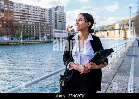 Contenu ethnique femme entrepreneur en tenue formelle avec dossier et sac à bandoulière pour regarder en ville Banque D'Images