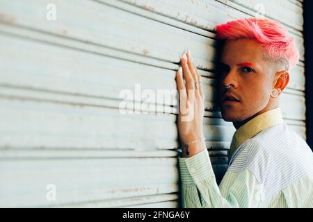 Vue latérale du jeune homme transgenre en chemise rayée avec coupe moderne en regardant l'appareil photo sur fond gris Banque D'Images